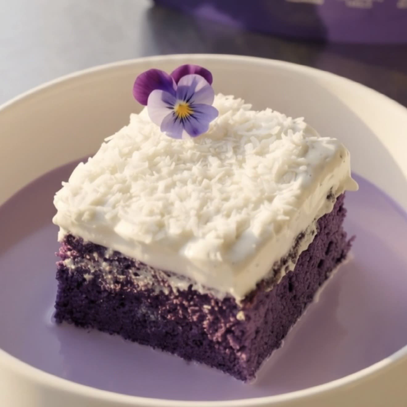 Stykke ube-kokos tres leches-kage toppet med kokosflødeskum og revet kokos, klar til servering | Ube Nolia