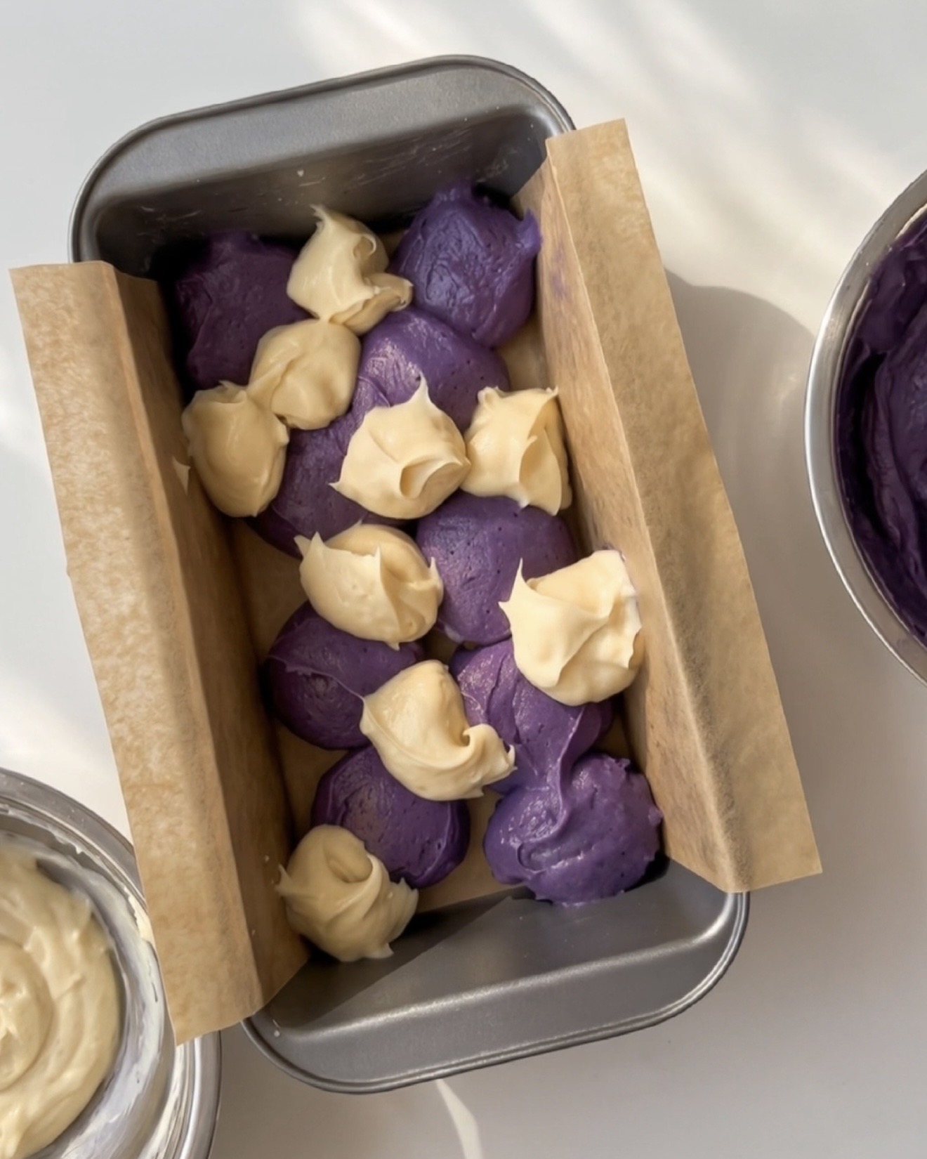 Skefulde lilla ube-dej og vaniljedej skiftevis i en beklædt brødform til Ube Nolia ube marble pound cake