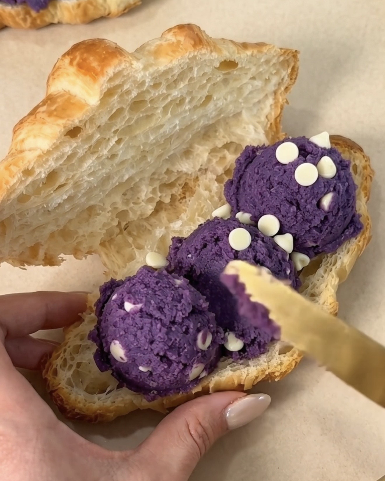Fordeling af UBE NOLIA lilla ube (lilla yam) hvid chokolade chip cookie dej skefulde inde i en skåret smør-bagericroissant for at lave en ube crookie