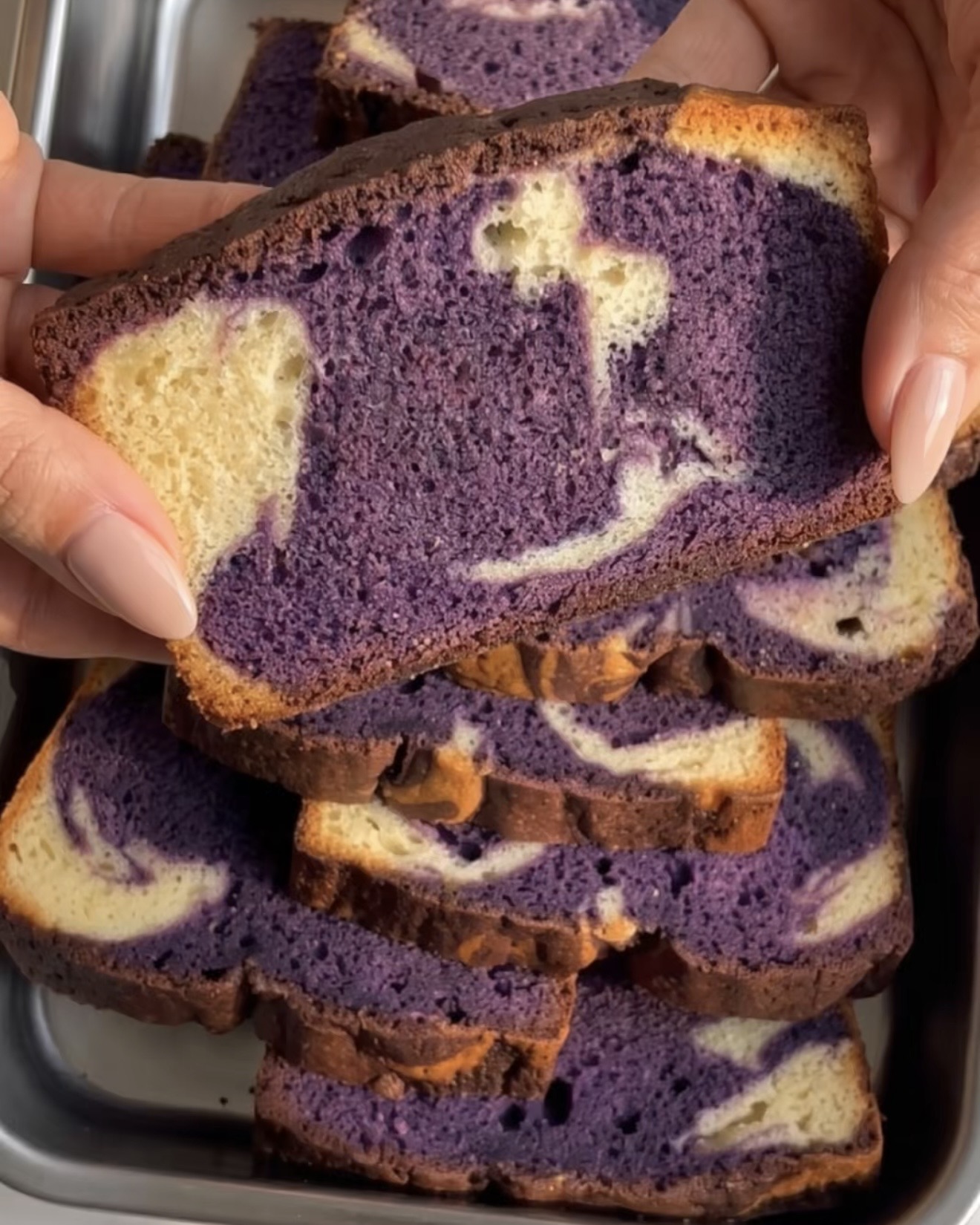 Hånd der holder et stykke ube marmor pound cake med en lilla og vaniljehvirvel, bagt med Ube Nolia ubepulver