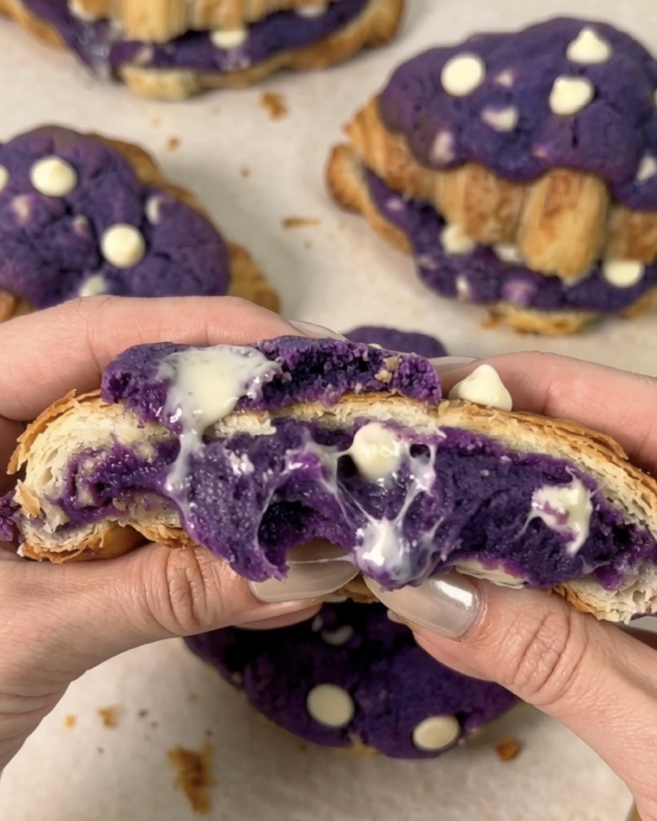 Friskbagte UBE NOLIA ube crookies trukket fra hinanden for at afsløre et smeltet lilla ube (lilla yam) hvid chokolade cookie center, der flyder mellem gyldne croissantlag