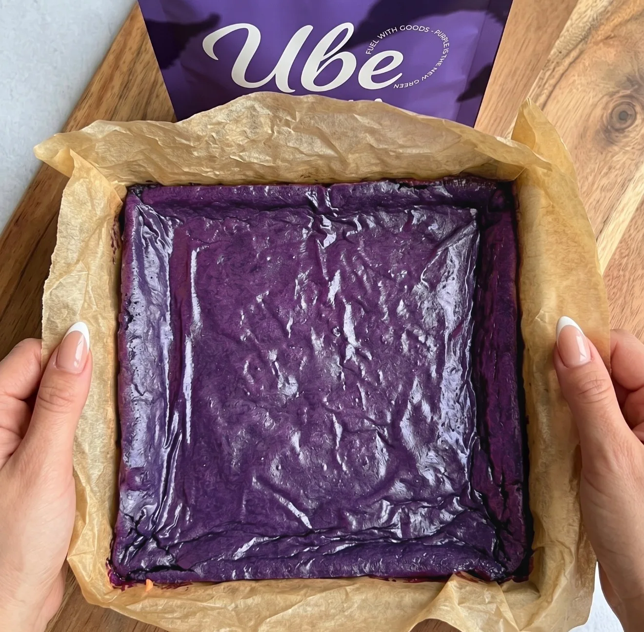 Dyblilla ube brownie dej lagdelt i en bagepapirbeklædt firkantet form ved siden af en Ube Nolia powder pose
