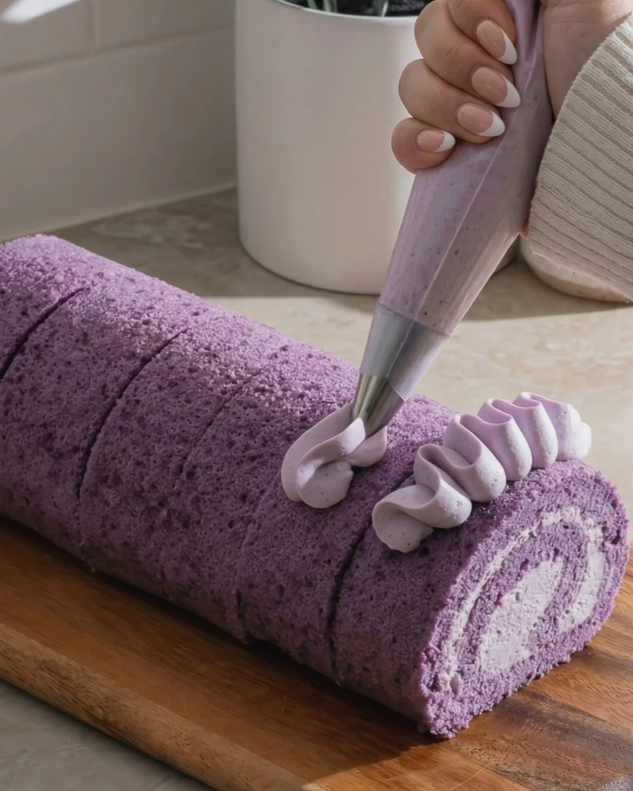 Sprøjter dekorative ube flødeskumsrosetter på toppen af den færdige lilla ube roulade af Ube Nolia