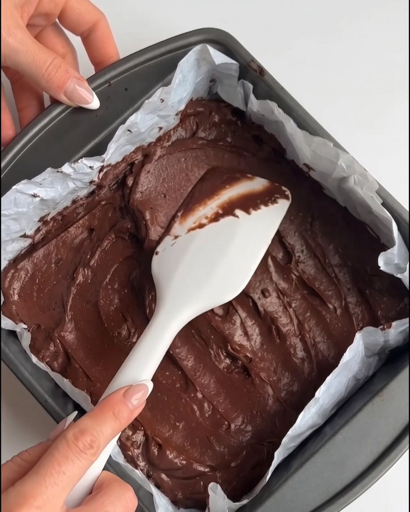 Glat Ube Dubai chokolade brownie dej spredt i en bagepapirbeklædt firkantet form, klar til at blive bagt til Ube Nolia opskriften